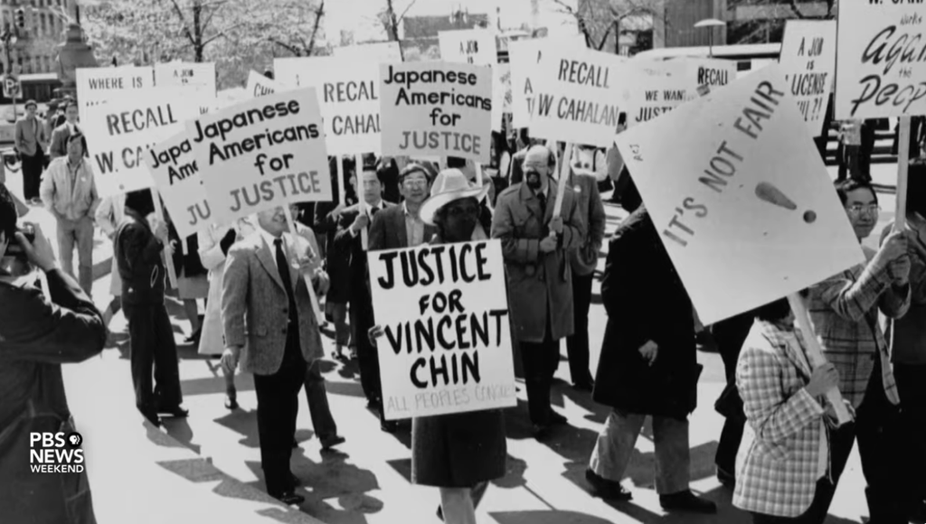 Black and white photo of a protest march with people holding signs that read 'Justice for Vincent Chin,' 'Japanese Americans for Justice,' and 'It's Not Fair!' The image captures a moment of activism and solidarity within the Asian American community seeking justice for Vincent Chin. #PBSNewsWeekend