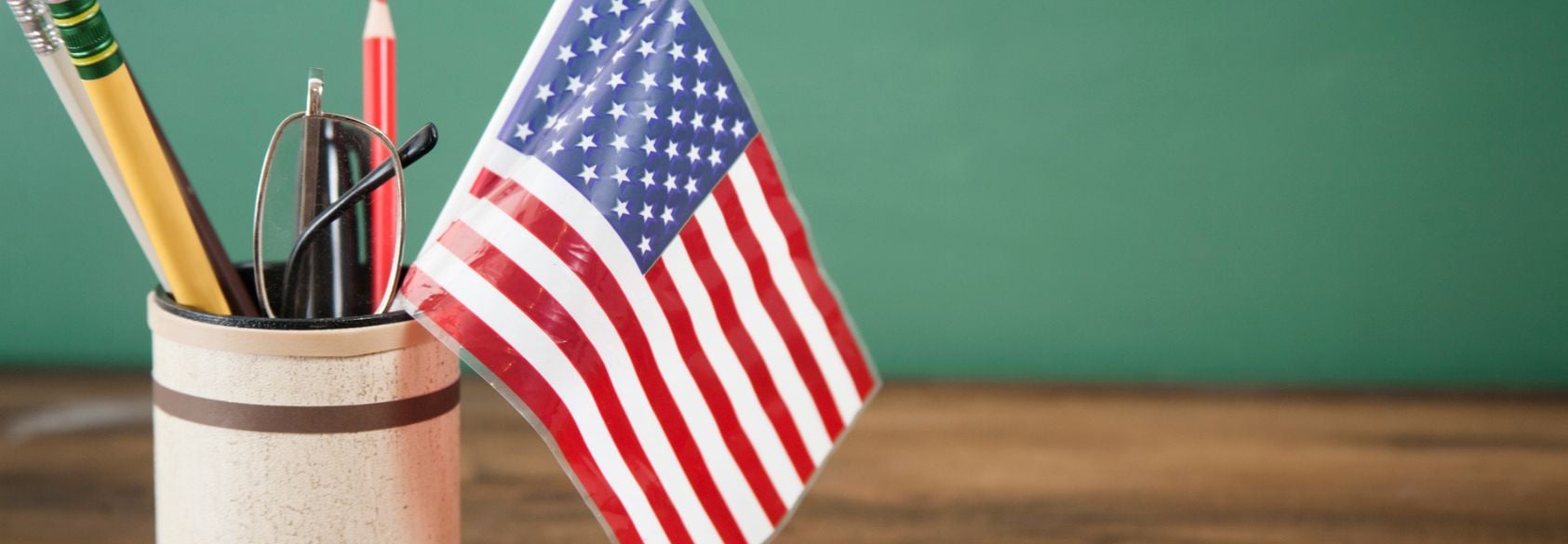 A small American flag in a pencil holder next to school supplies, symbolizing debates over how U.S. history is taught in classrooms.