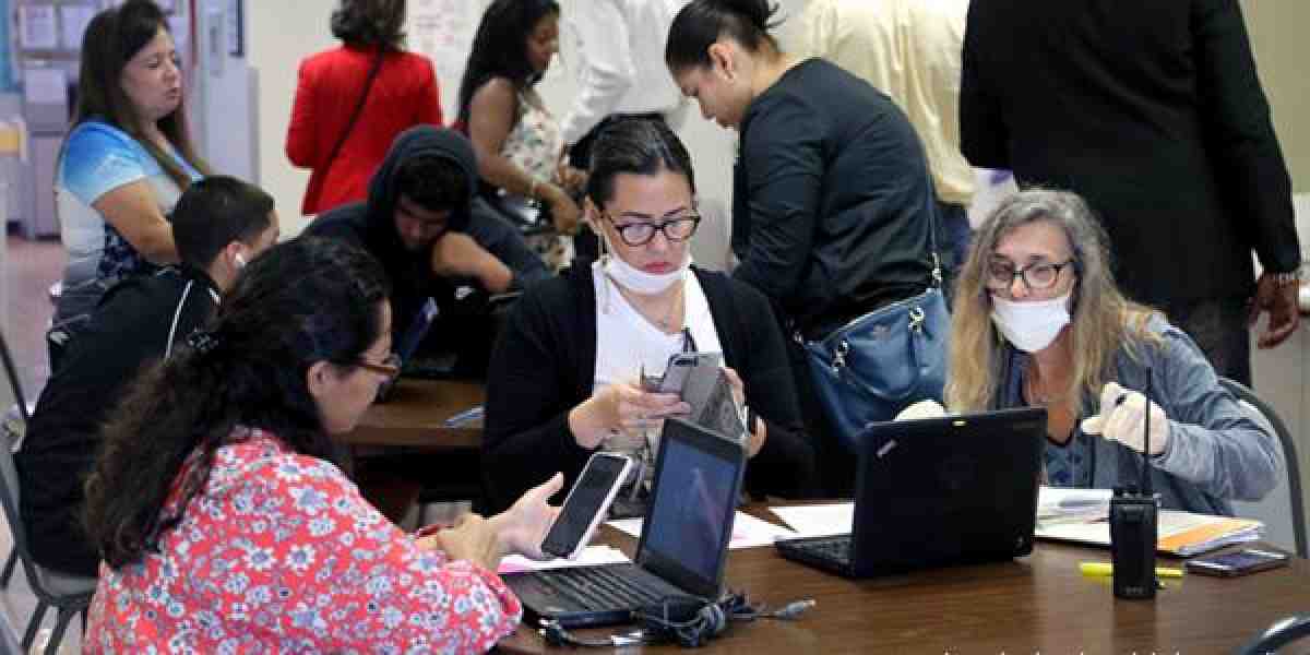 educaitonal inequities in schools: Carole D'Ausillo, an ESE Specialist (right) at a Broward County, Fla., middle school, helps parents and students with the distribution of computer devices for students. (Mike Stocker/South Florida Sentinel)